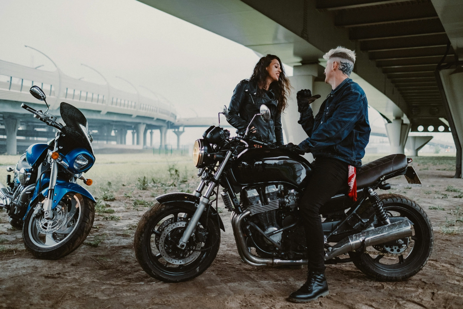 Fahrschule Fahrwerk Bayer GmbH - Führerscheinausbildung - Ein Mann und eine Frau stehen neben einem blauen und einem schwarzen Motorrad unter einer Brücke.